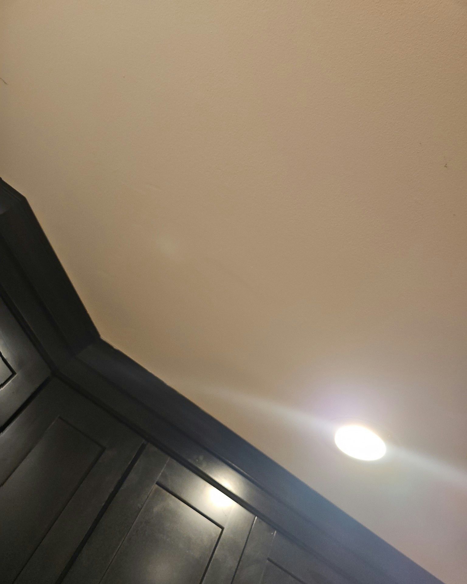 Dark cabinets angled against a beige ceiling with a recessed light shining in the corner.