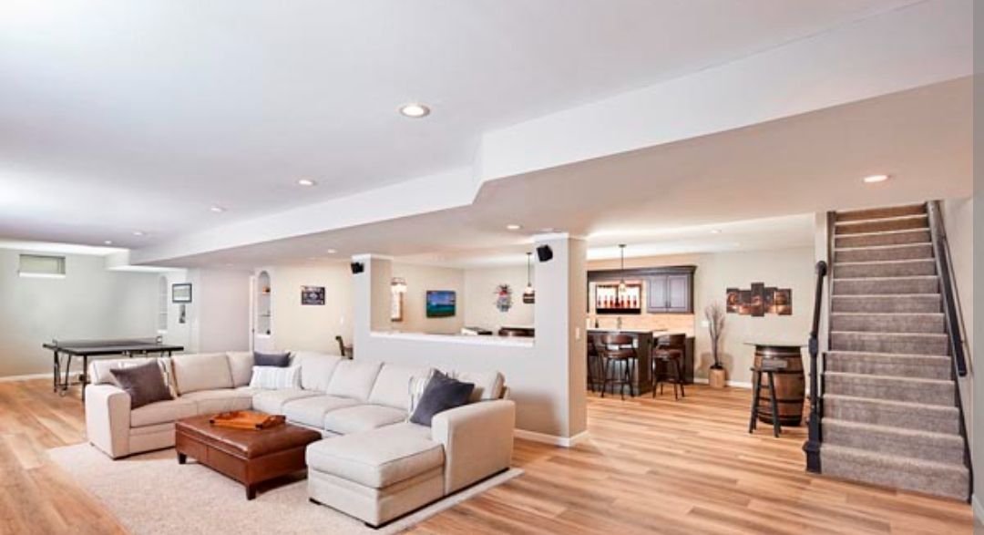 Spacious finished basement with sectional sofa, bar area, pool table, and stairs leading up.