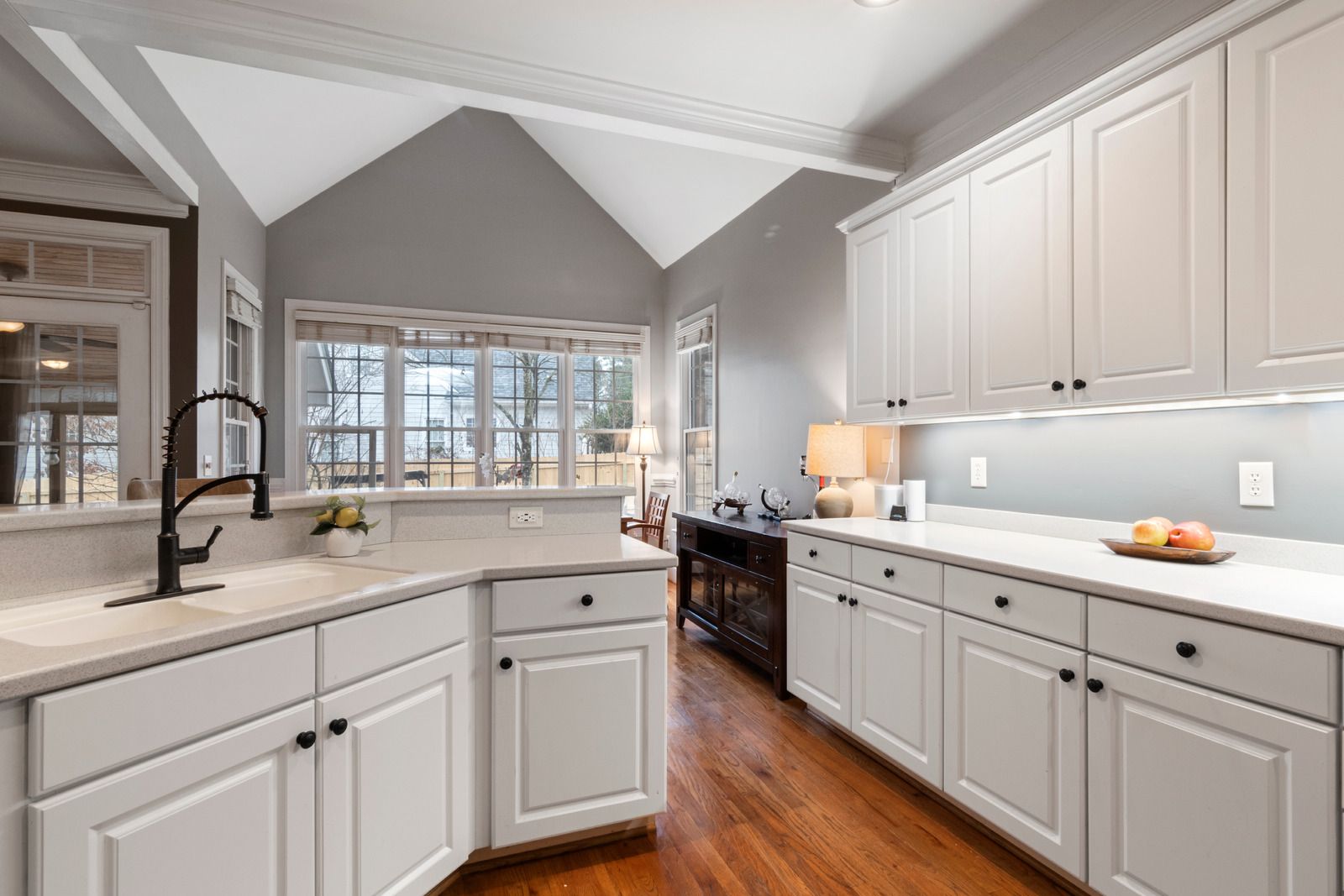 White kitchen with cabinets, countertops, and dark hardware. Hardwood floors, window, and grey walls.