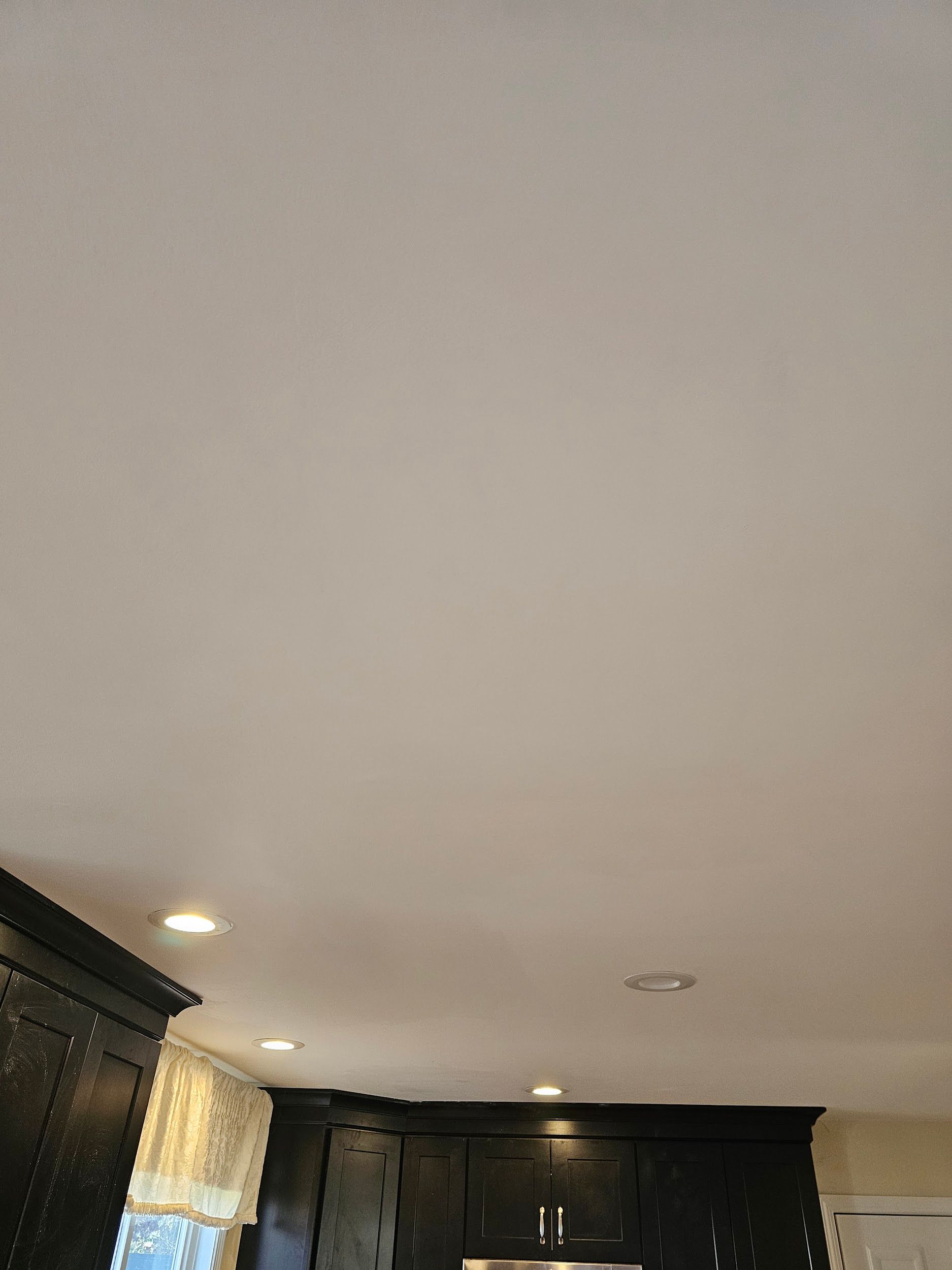View of a kitchen ceiling and dark cabinets. Recessed lighting is visible, and a window is partially seen.