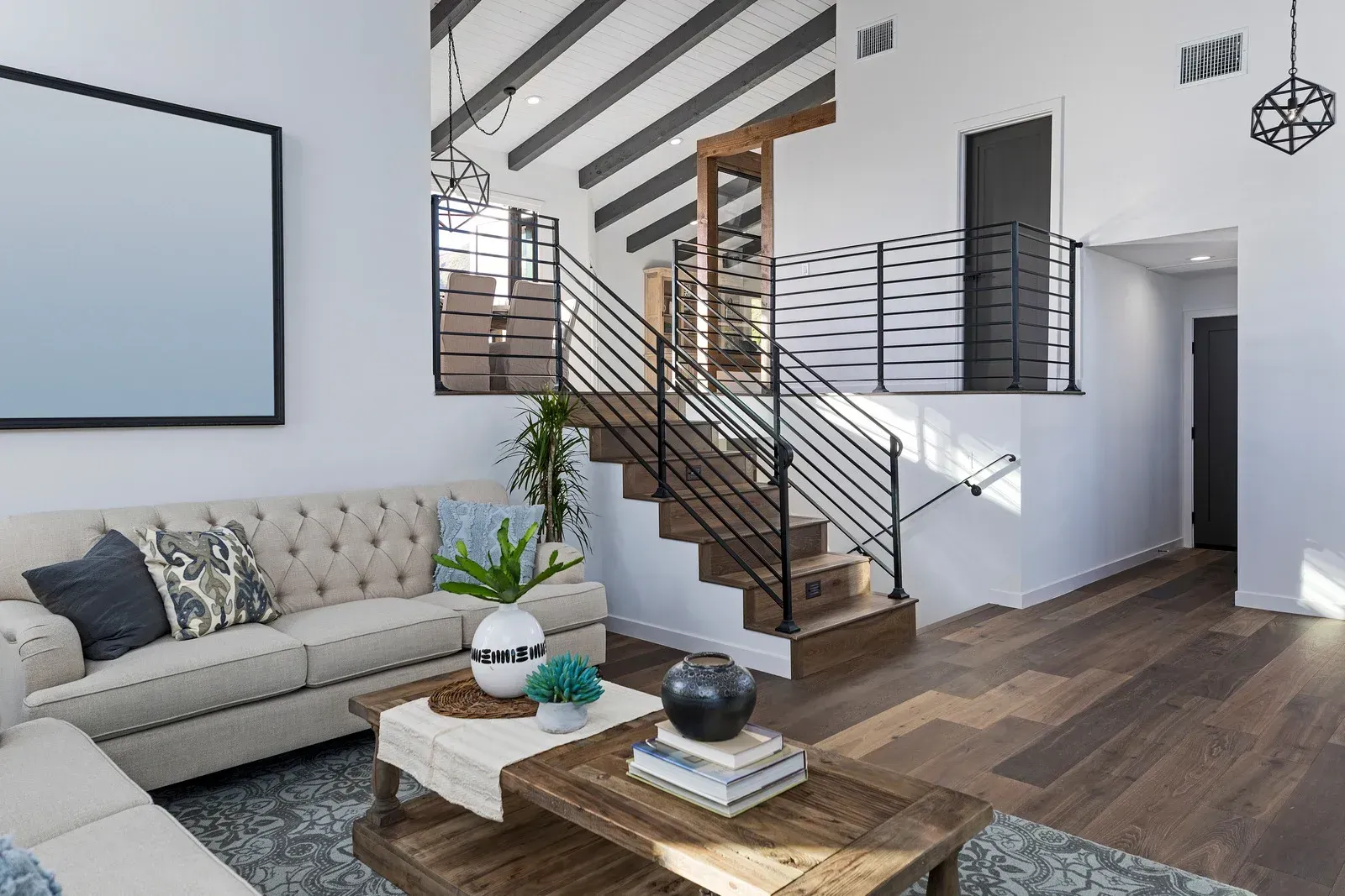 Living room with staircase, sofa, coffee table, wood floor, white walls, black and white accents.
