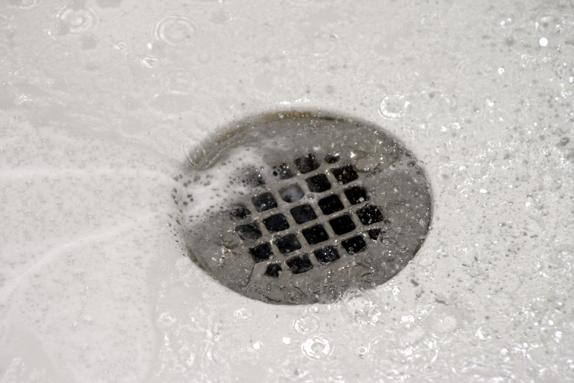 Person in blue work clothes using a snake tool to clear a sewer drain, outdoors.