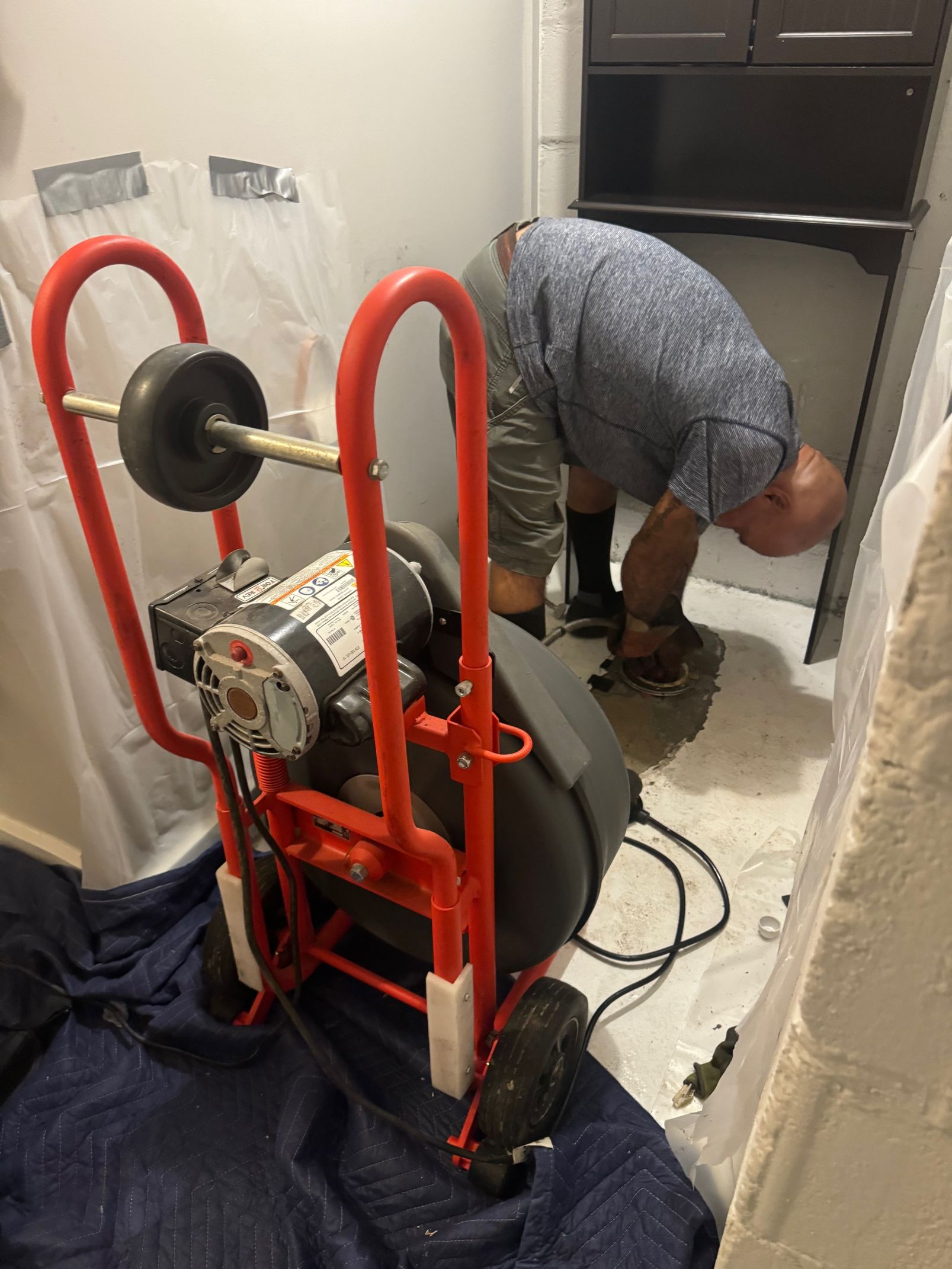 Person using a sewer camera to inspect a manhole on a paved street. The camera has a built-in monitor.