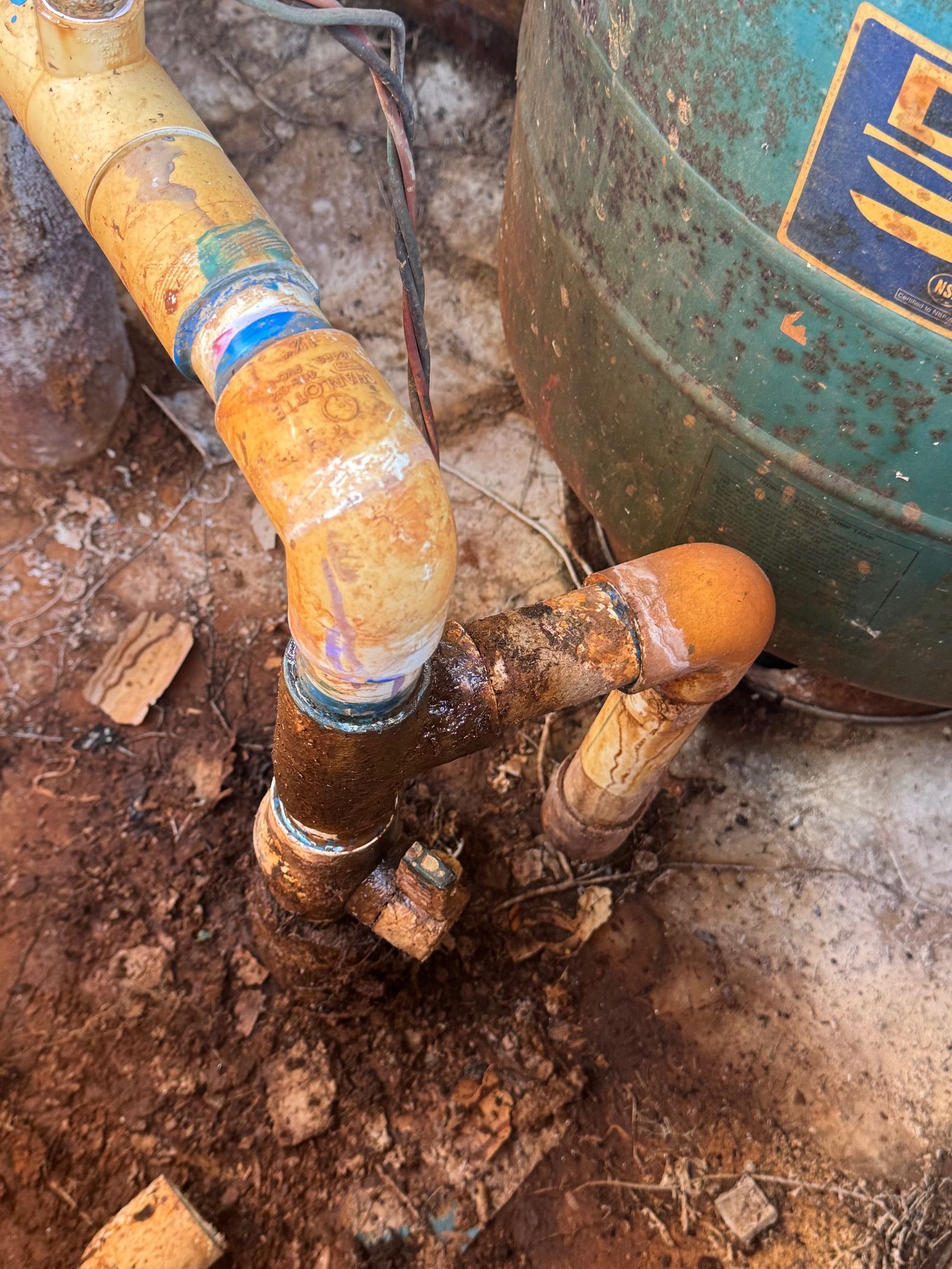 Yellow PVC pipes with brown stains connected in dirt near a green metal container.