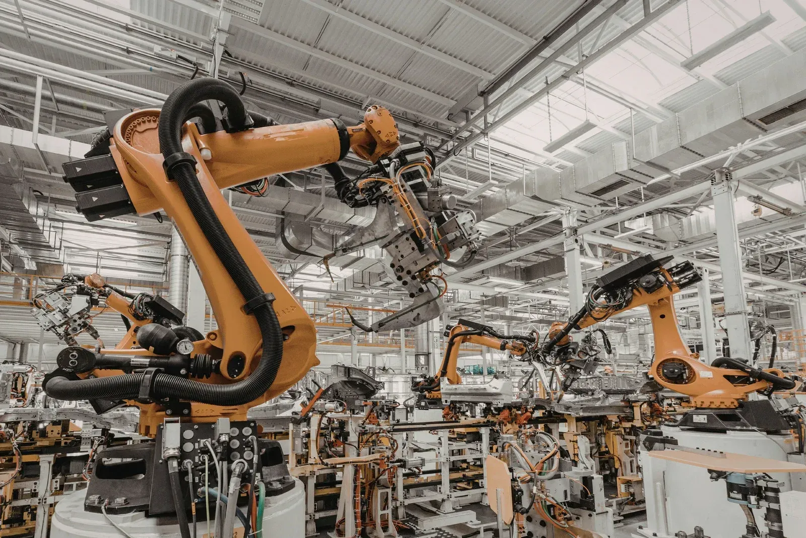 Robotic arms welding and assembling parts in a factory. Orange and gray machines, bright interior.
