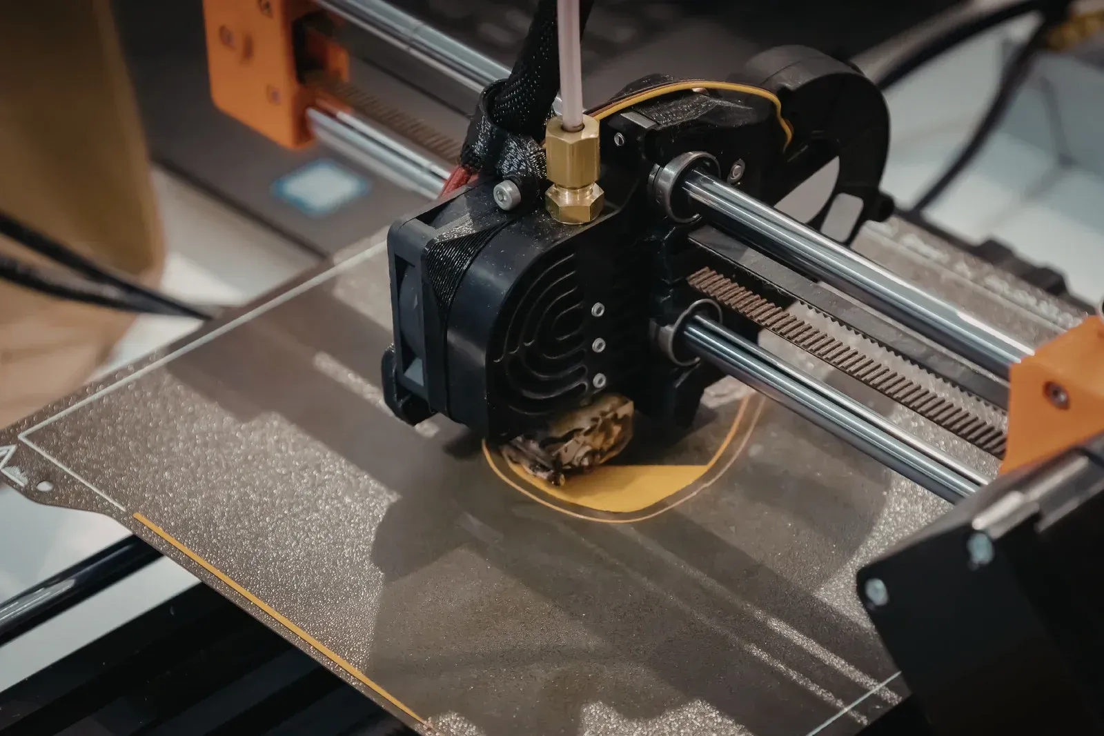 3D printer head depositing molten plastic onto a heated bed, creating a yellow disc.