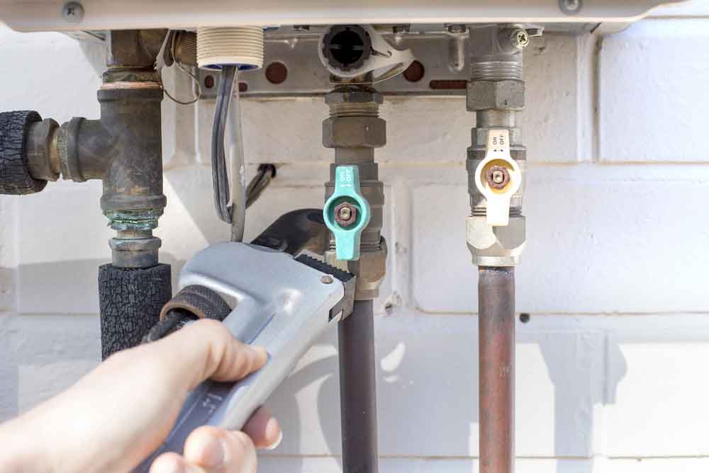 A Person is Fixing a Water Heater With a Wrench — Cape Byron Plumbing in Lennox Head, NSW