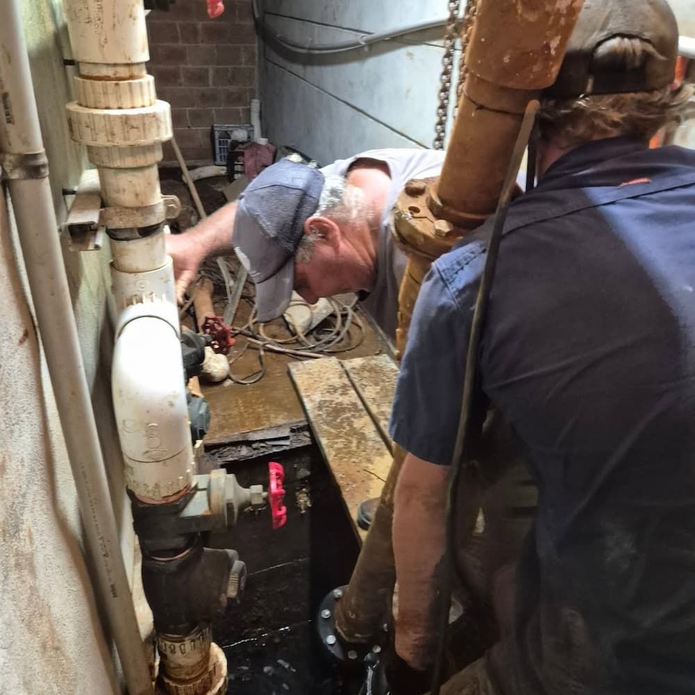 Two Workers in Casual Attire Repair a Large Pipe in a Dimly Lit