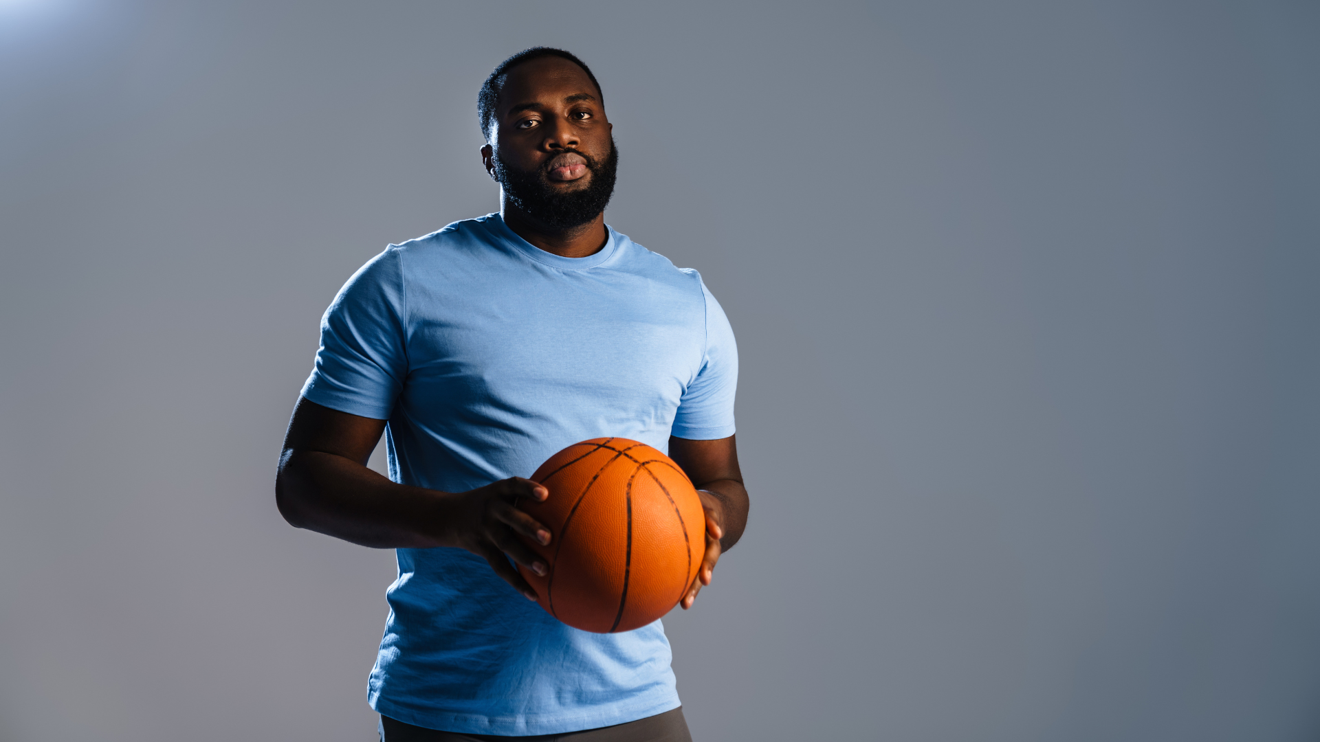 A man in a blue shirt is holding a basketball in his hands.