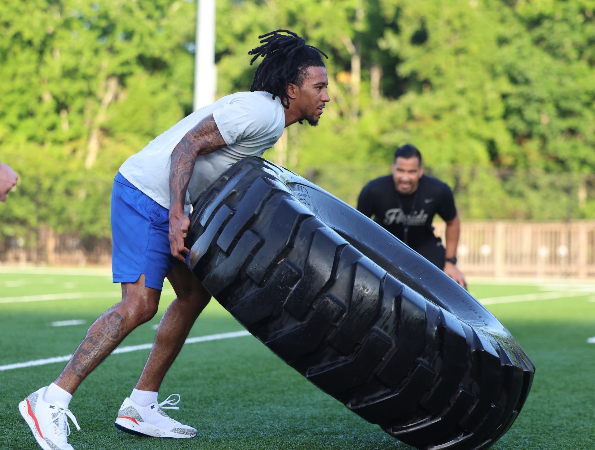 A man is pushing a large tire on a field.