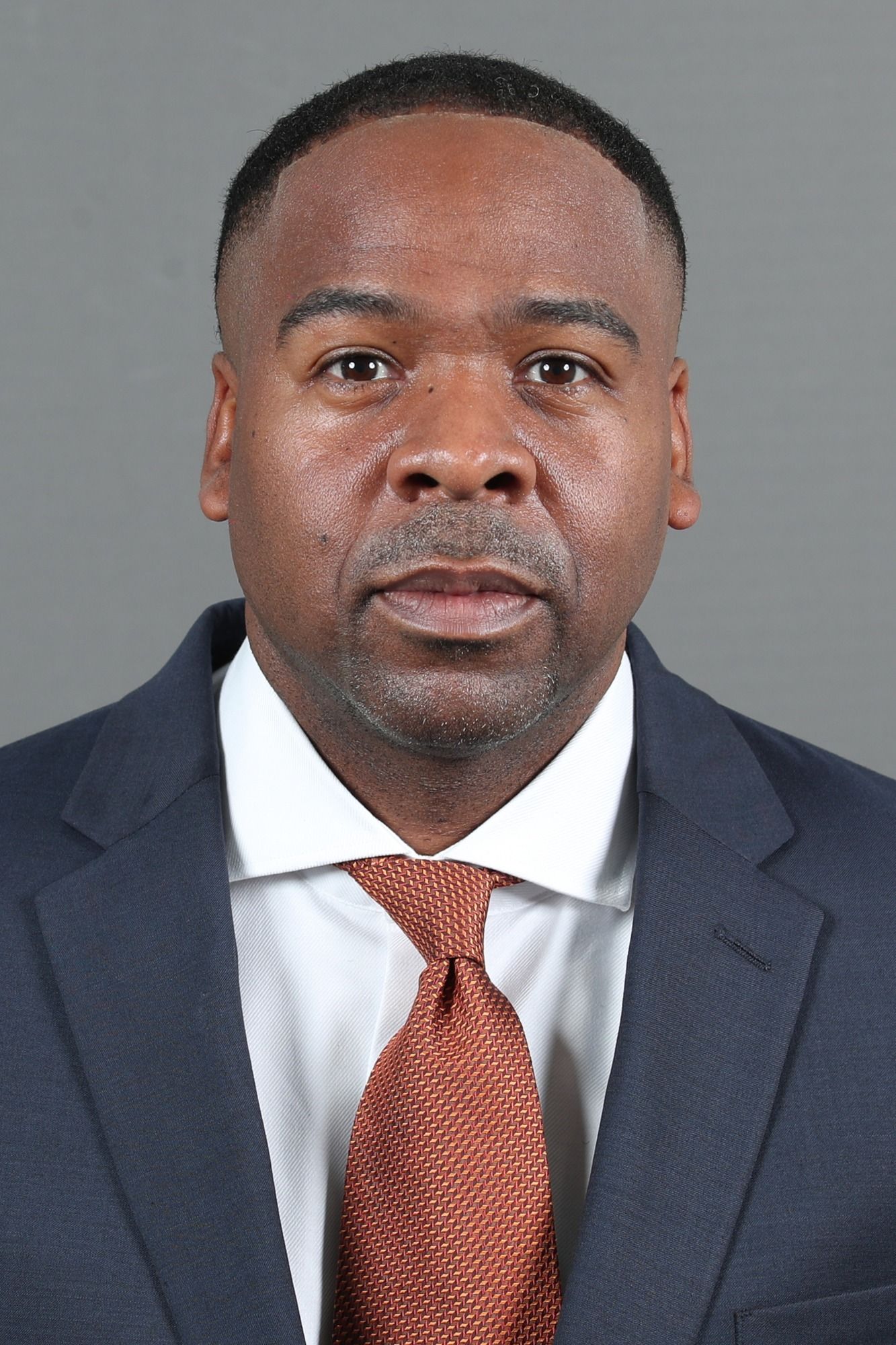 A man in a suit and tie is standing in front of a gray background.