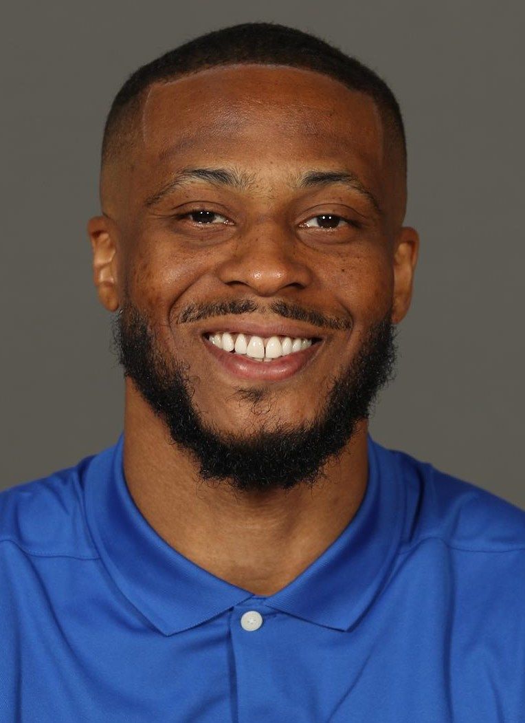 A man with a beard is wearing a blue shirt and smiling.