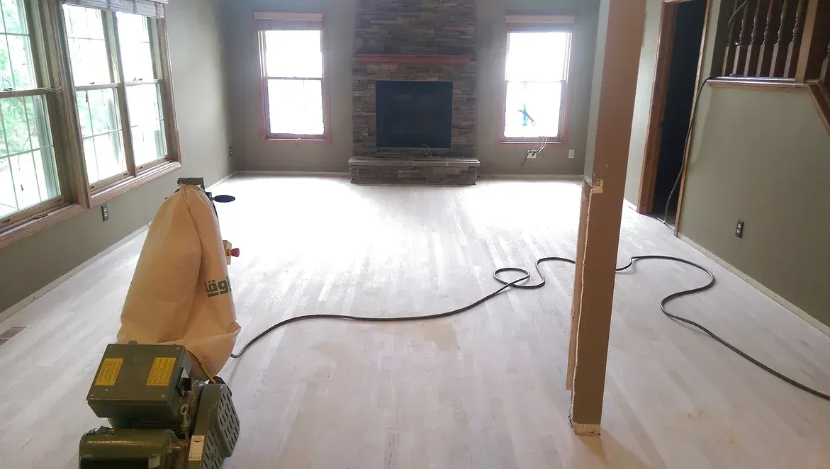 A machine is sanding a wooden floor in a living room.