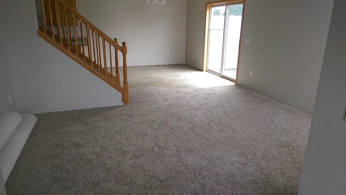An empty living room with a staircase and a sliding glass door.