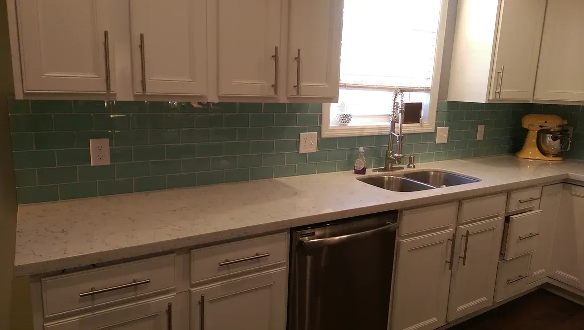 A kitchen with white cabinets , a sink , a dishwasher , and a window.