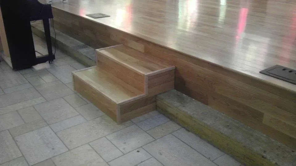 A wooden stage with stairs leading up to it and a piano in the background.