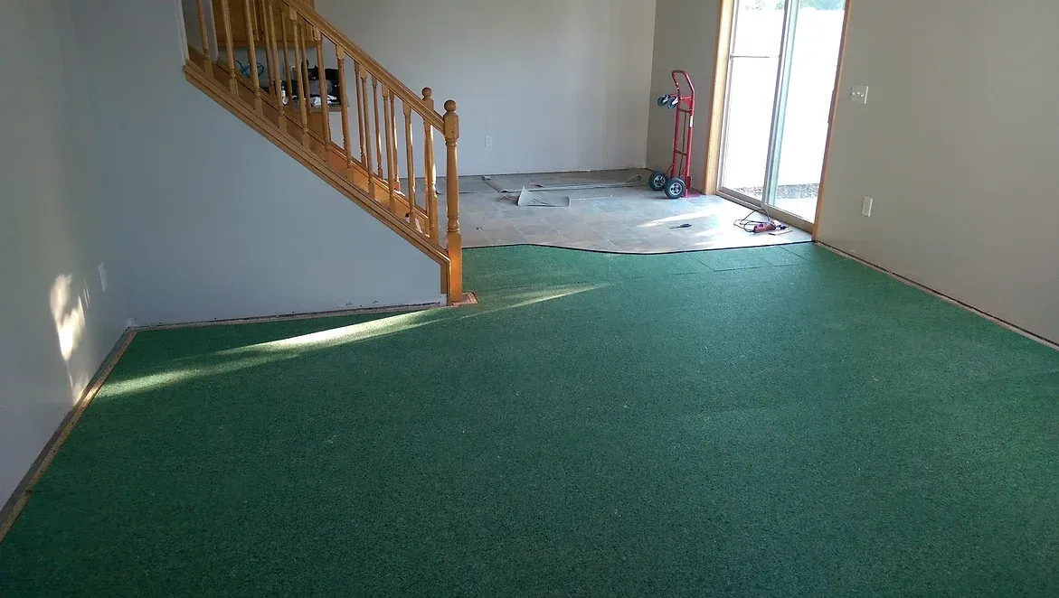 A living room with a green carpet and stairs.