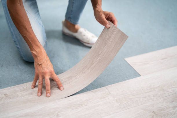 A person is laying a piece of vinyl flooring on the floor.
