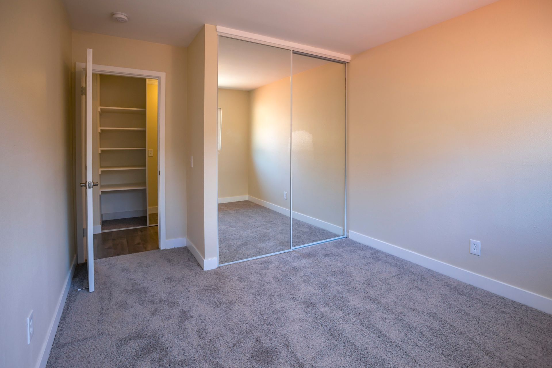 An empty bedroom with a closet and a large mirror.