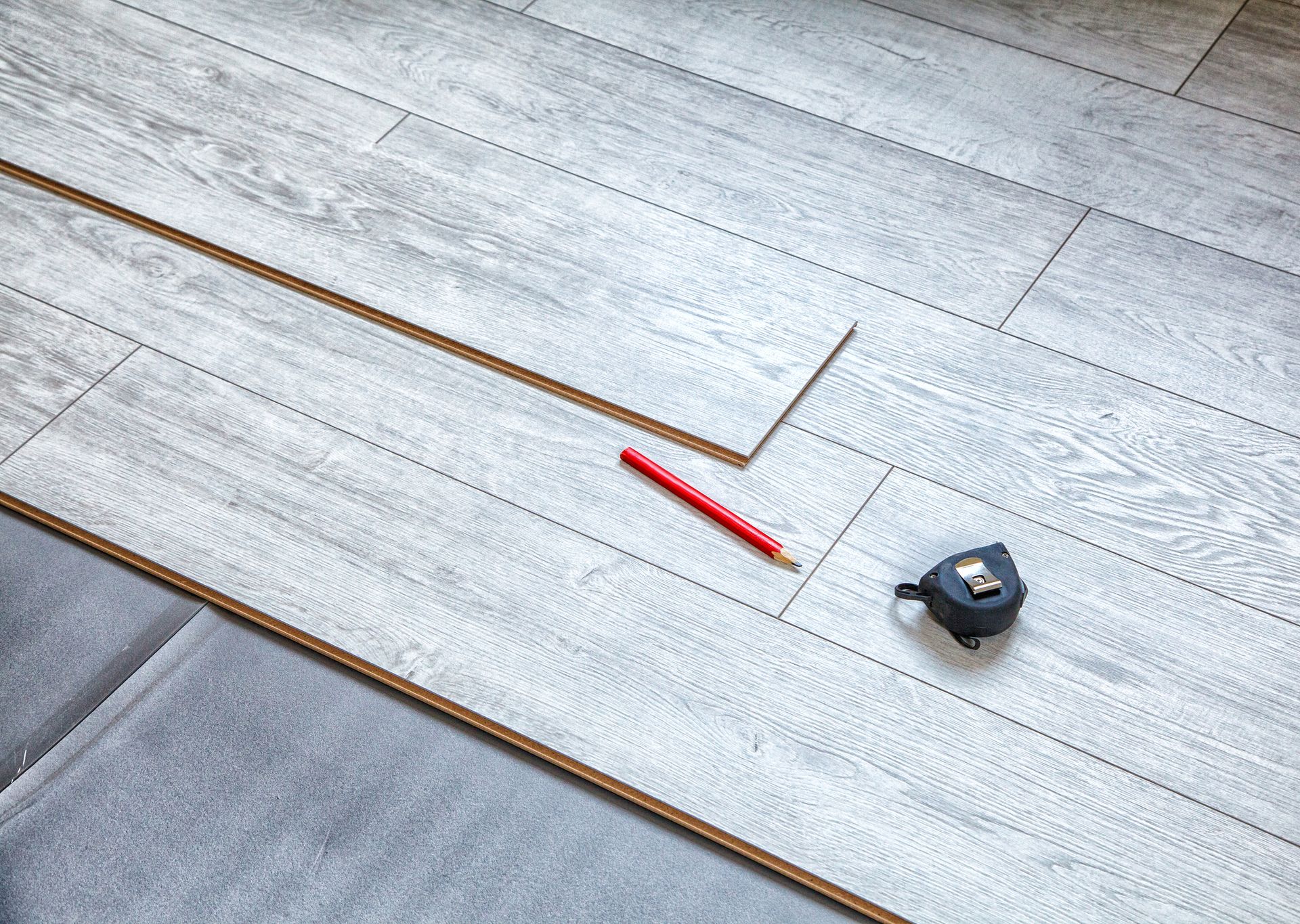 A wooden floor with a tape measure and a pencil on it.