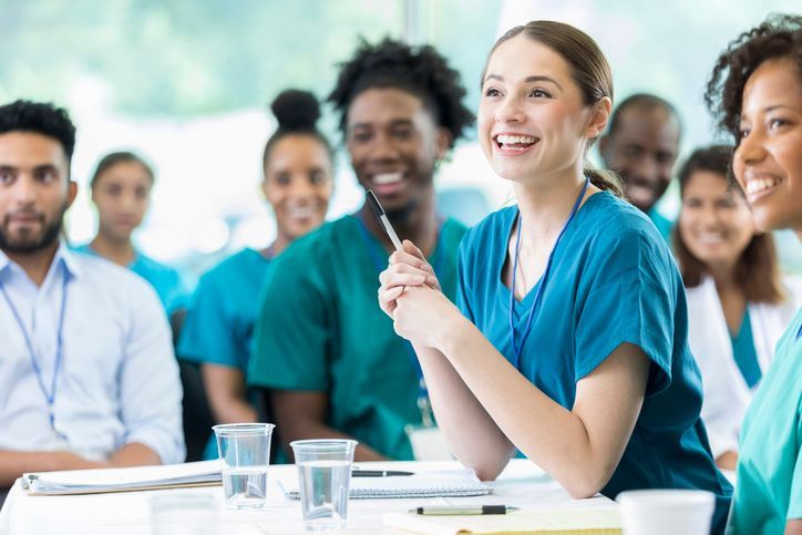 A group of nurses are sitting at a table having a meeting.