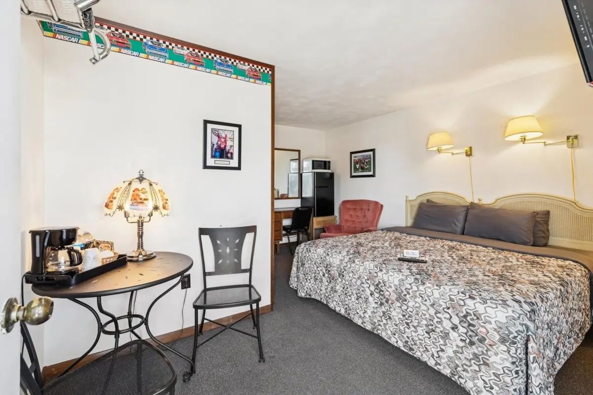 Cozy bedroom with floral bedspread, small table and chairs, lamps, and a mirror above the bed