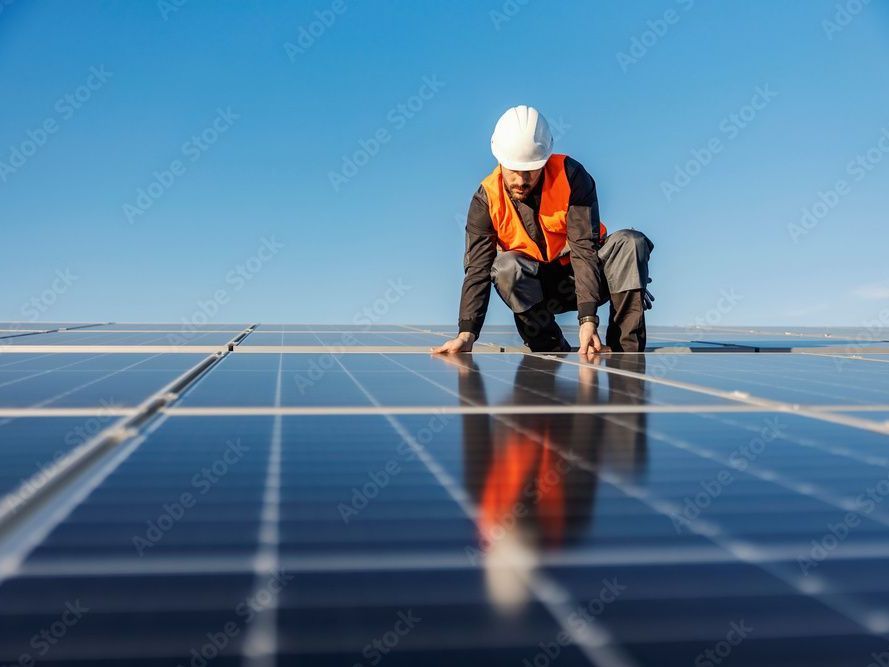 A man is kneeling on top of a solar panel.