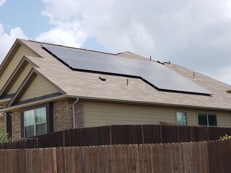 A house with solar panels on the roof is behind a wooden fence.