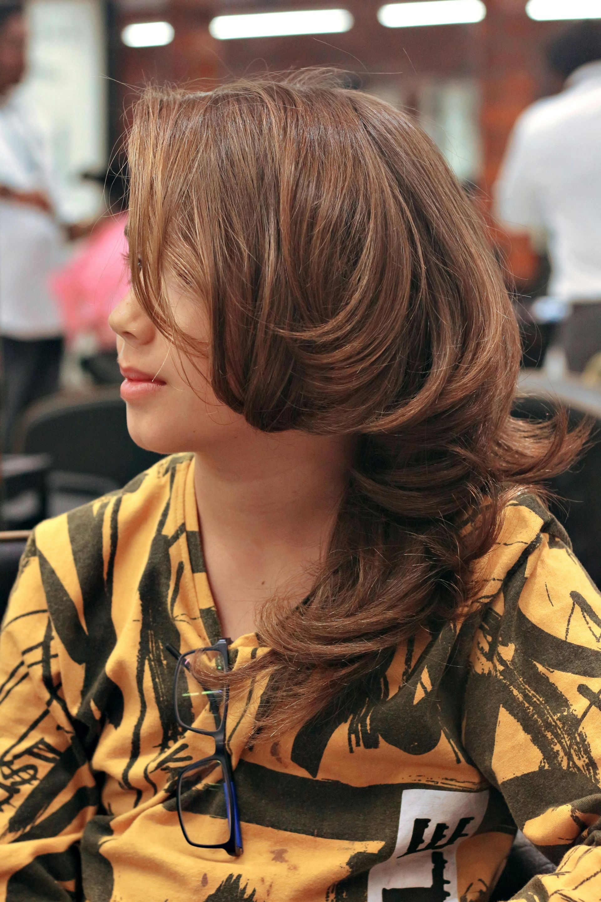 Woman with layered brown hair and yellow and black patterned shirt in a salon.