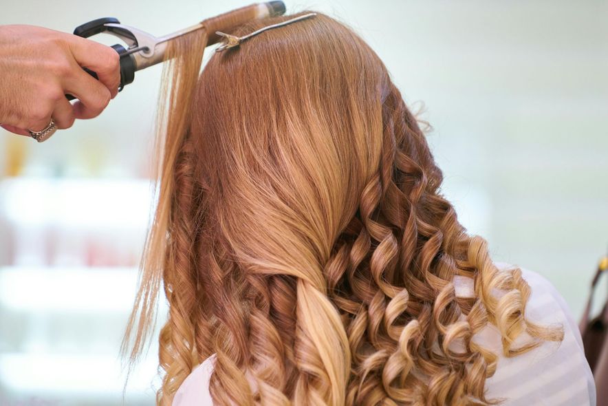 Person's hair being curled with a curling iron, transitioning from straight to bouncy curls.