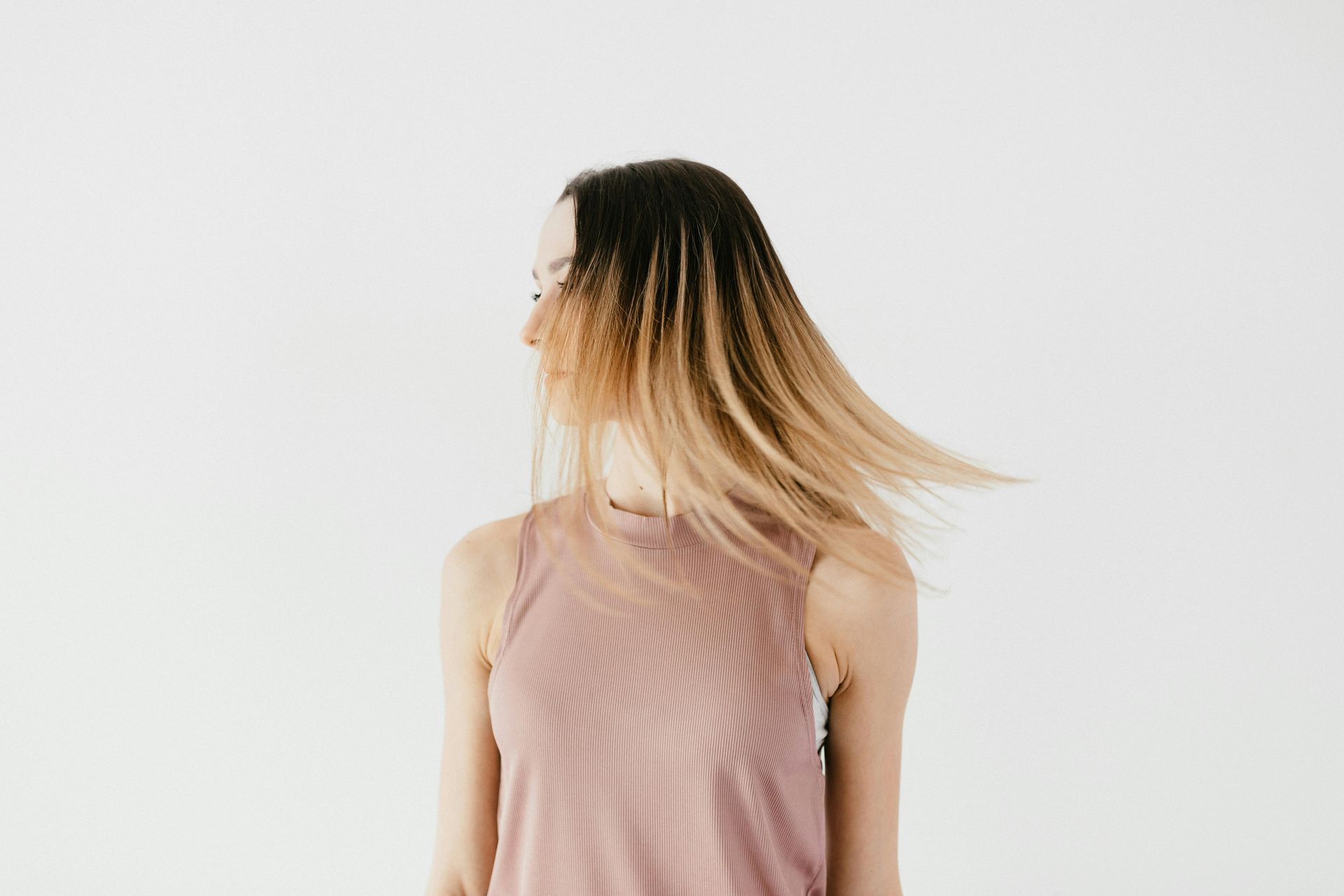 Woman with ombre hair, in a pink tank top, turning her head against a white background.
