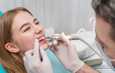 A dentist using a handpiece to clean a patient's teeth in a clinical setting.