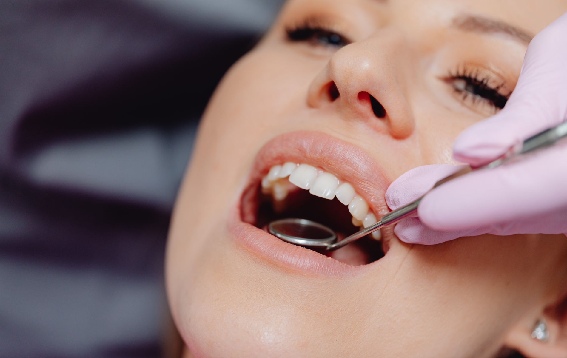 A dental practitioner in pink gloves uses a mirror to examine a patient’s teeth during a dental check-up.