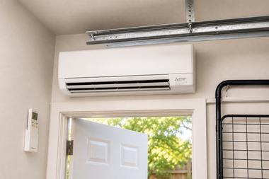 Wall-mounted white air conditioner above an open door in a garage-like room