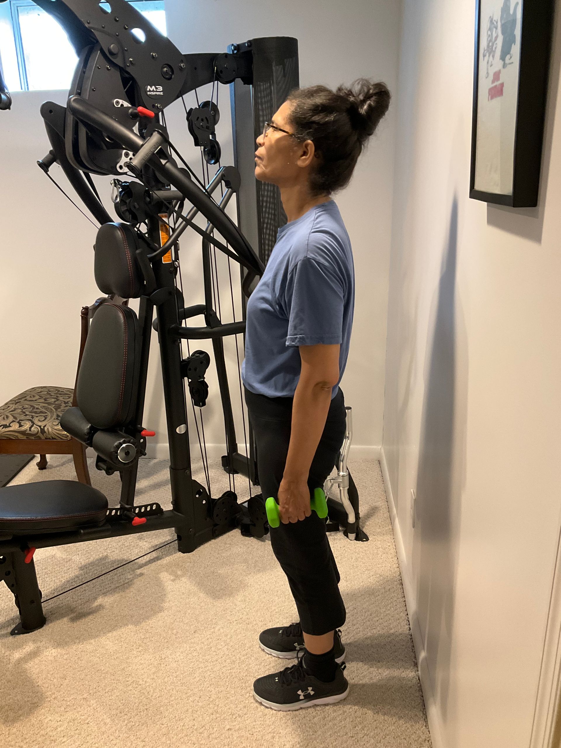 Woman standing with a dumbbell in her hand in a gym. She is in front of a weight machine.