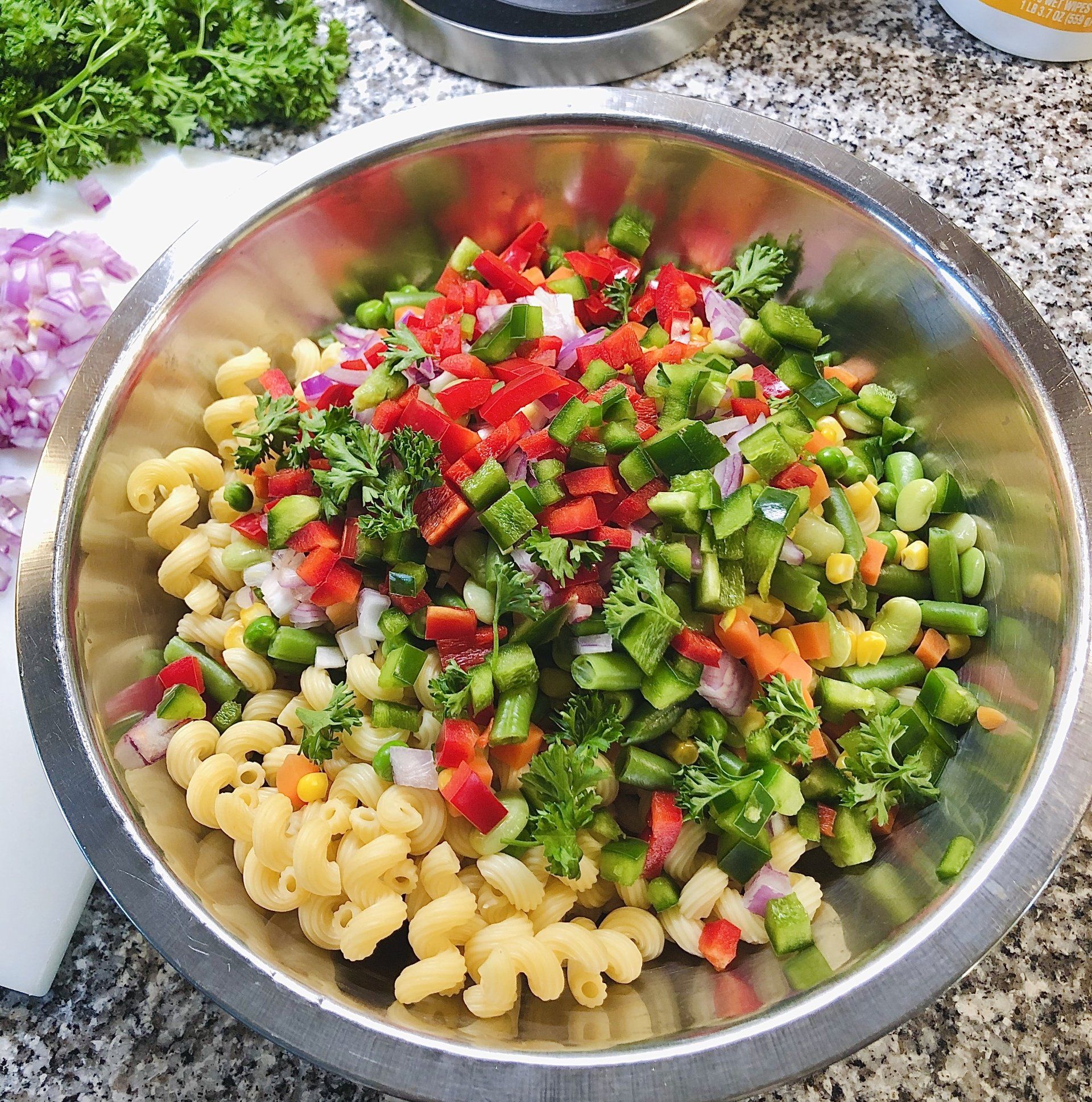 Pasta salad in stainless steel bowl, with chopped peppers, onions, and parsley.