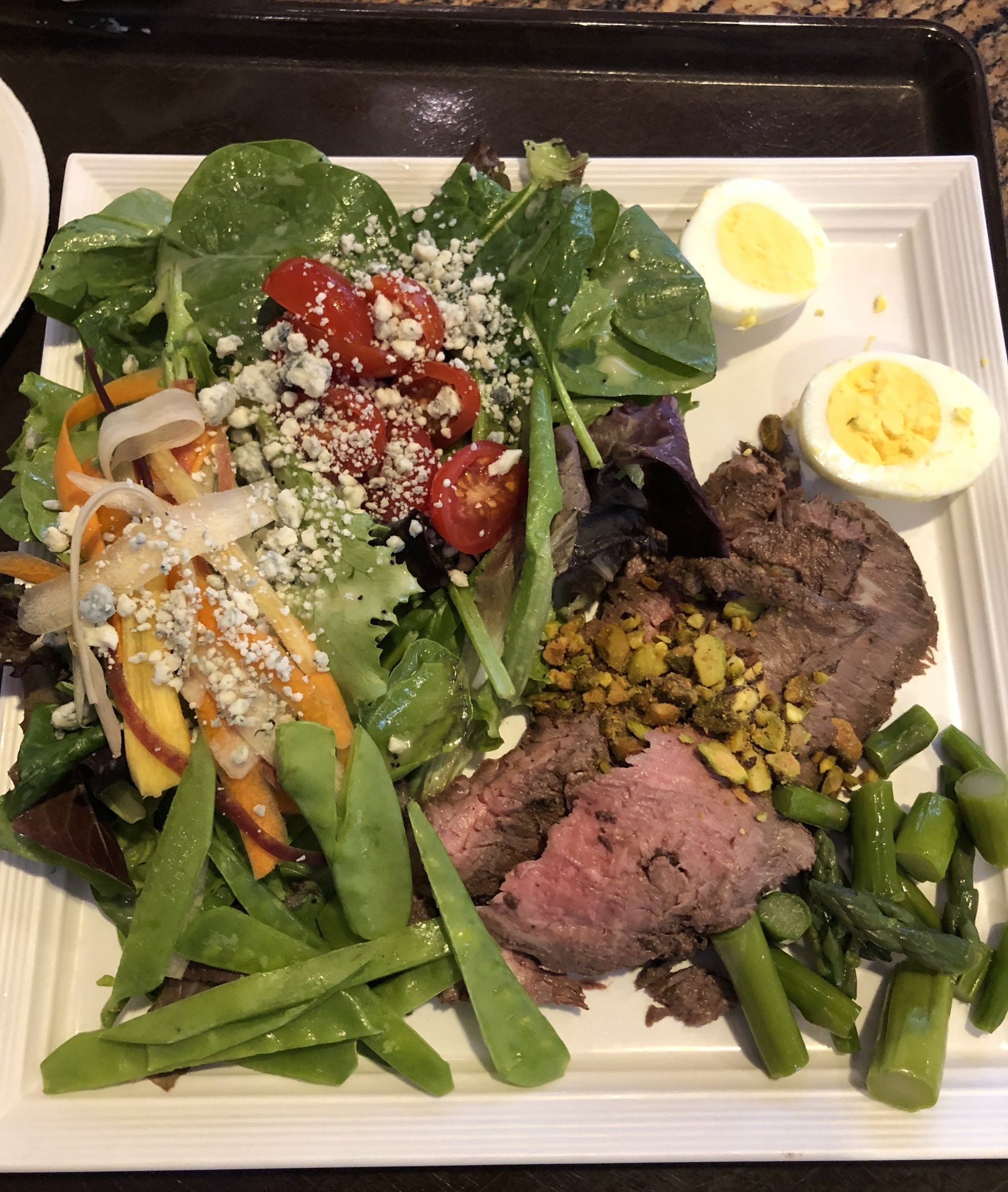 Plate of food: steak, salad with tomatoes, snap peas, eggs, asparagus, and pistachios.