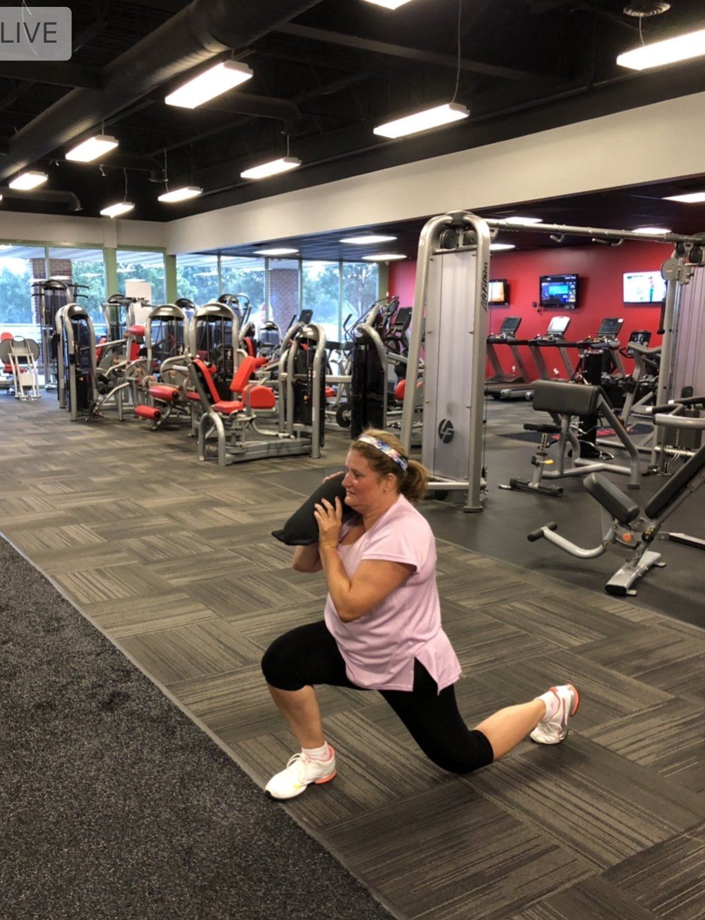 Woman in gym doing a weighted lunge, holding sandbag.