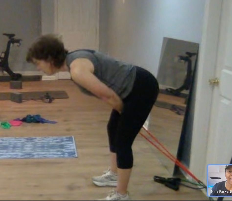 Woman doing a hamstring exercise with a resistance band, leaning forward, hands on hips. Indoor setting.