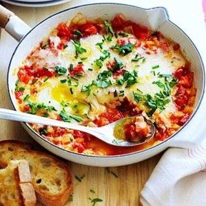 Shakshuka with eggs in a white pan, tomato sauce, herbs, served with bread.