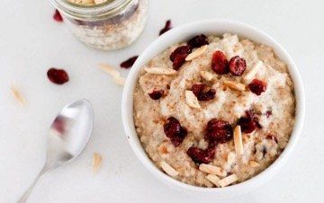 Oatmeal in white bowl with dried cranberries and sliced almonds. Jar of oatmeal mix and spoon beside.
