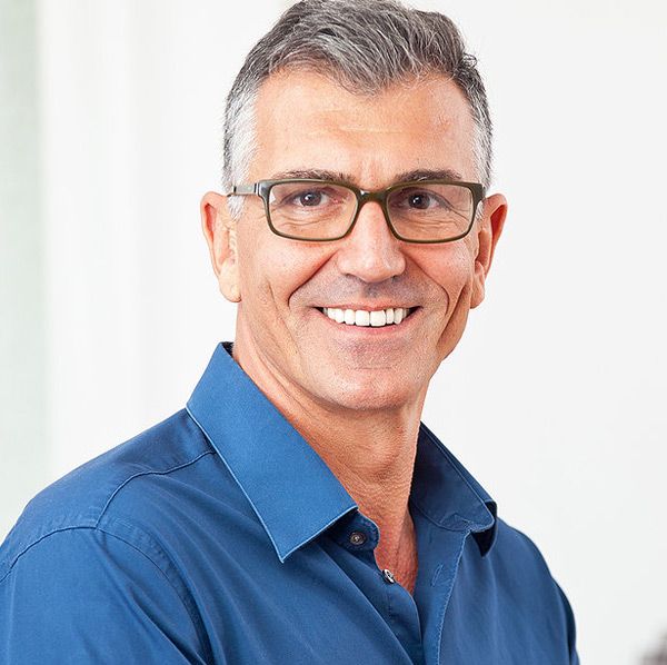 A man wearing glasses and a blue shirt smiles for the camera