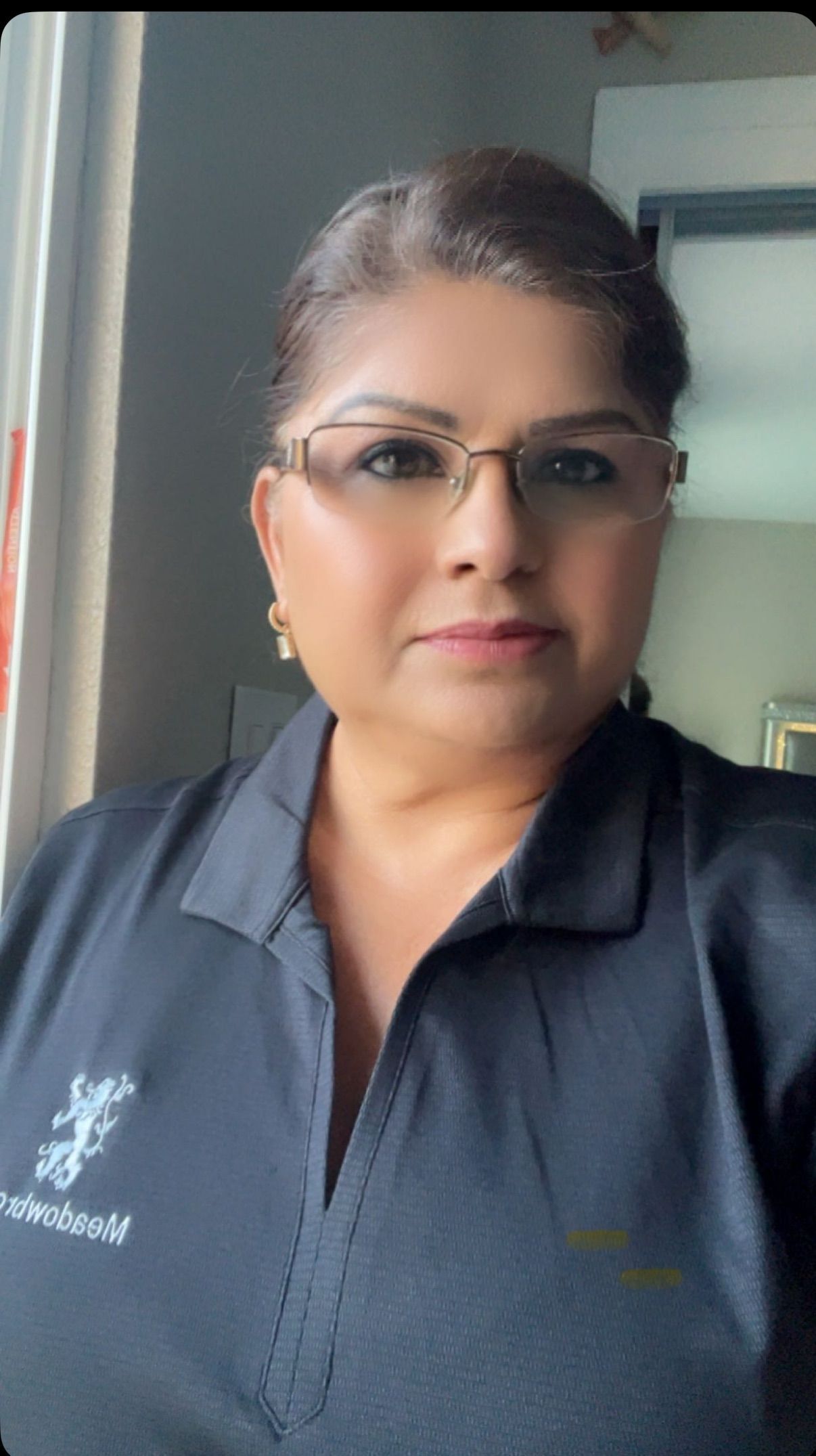 Woman in blue cardigan, arms crossed, standing outdoors in front of building and greenery.
