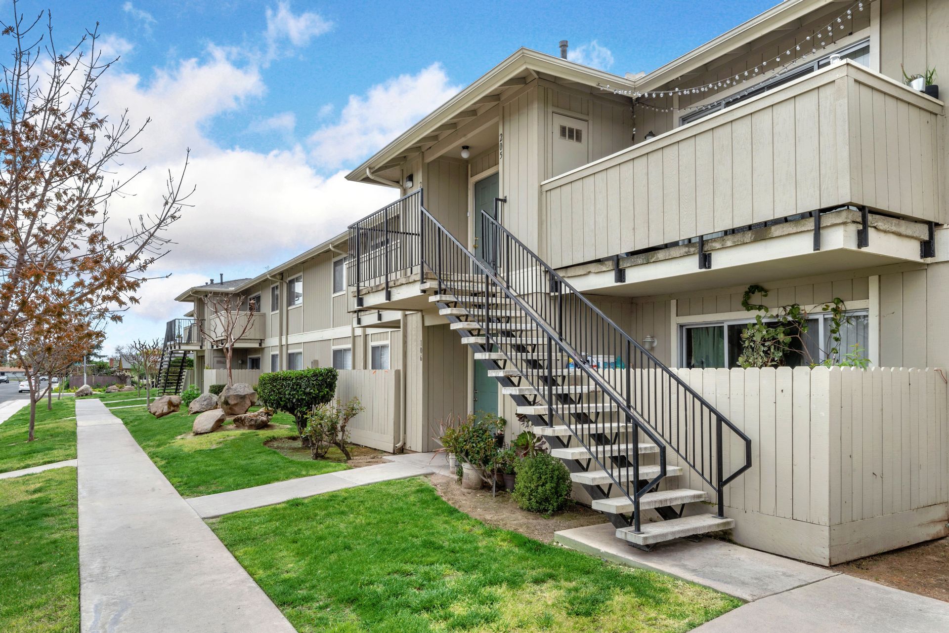 Apartment complex exterior with stairs, walkway, green lawn, and blue sky.