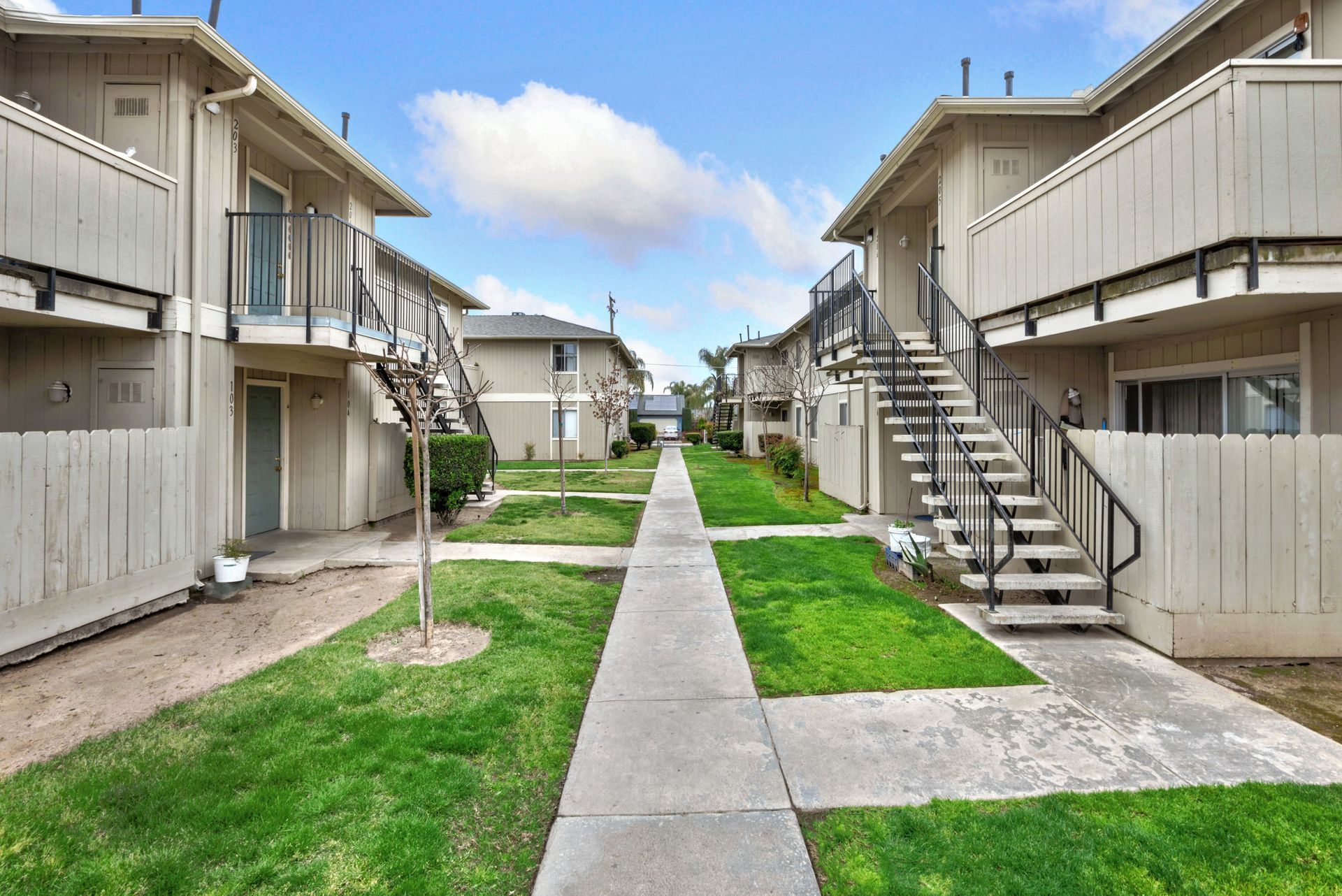 Apartment complex exterior with walkways, grass, and staircases leading to units.