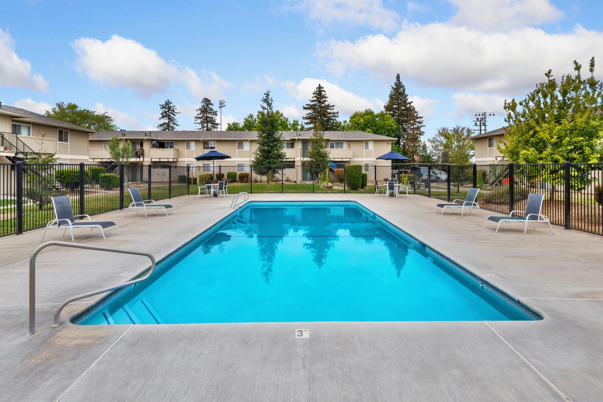 Swimming pool surrounded by lounge chairs, with a building in the background under a cloudy sky.