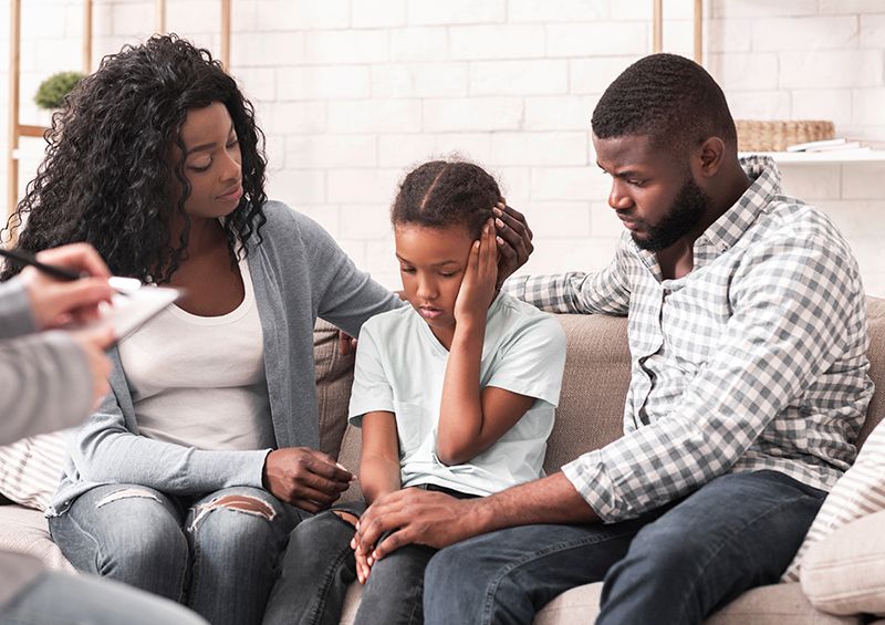 Family in therapy session, consoling child, seated on couch.