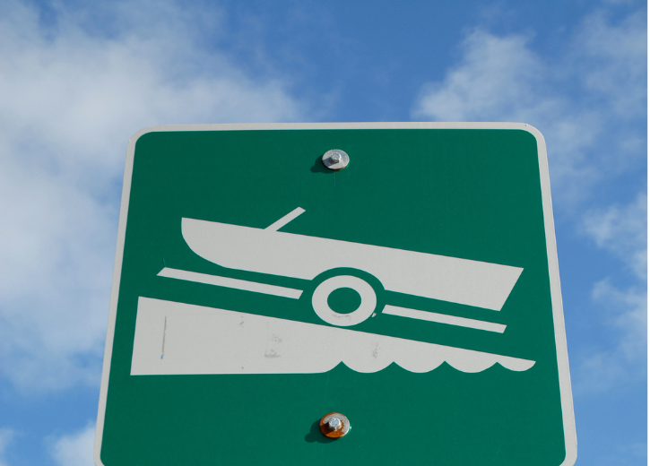 Green sign with a white graphic of a boat being launched into the water, indicating a boat ramp.