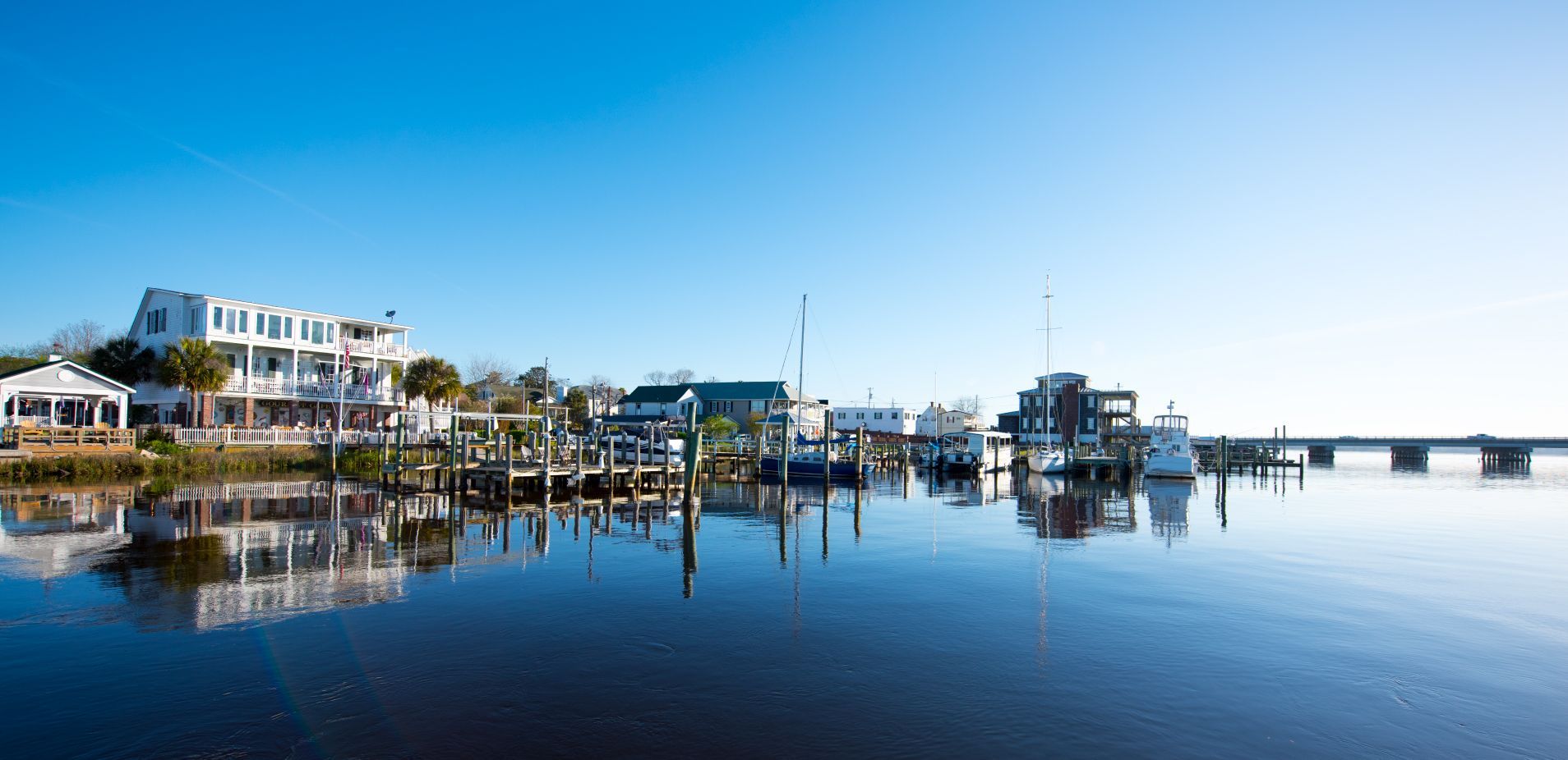 Waterfront with docks, buildings, and reflections under a clear blue sky.