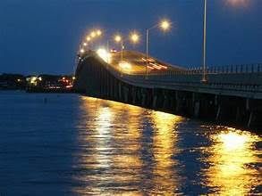 Bridge over water at night, lit by streetlights; cars driving on the bridge.